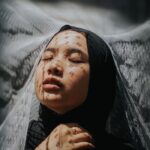 Emotive portrait of a woman with lace veil patterns in soft light.