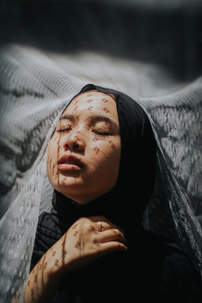 Emotive portrait of a woman with lace veil patterns in soft light.