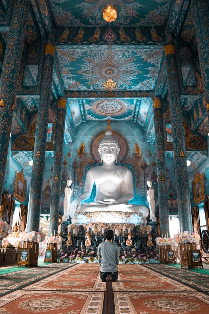 A serene view of a person worshipping inside the ornate Blue Temple of Chiang Rai, Thailand.